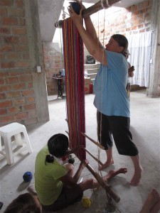 Passing ball of yarn front to back over upper loom bar. 